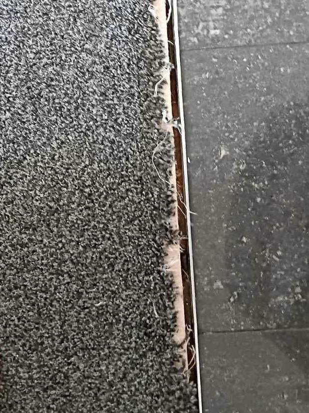 Close-up of the frayed carpet edge before it was re-fixed against the tile